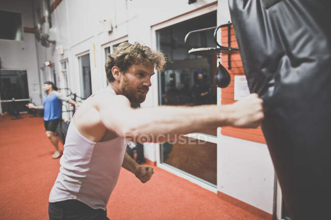 Boxer masculino usando saco de perfuração no ginásio — Fotografia de Stock