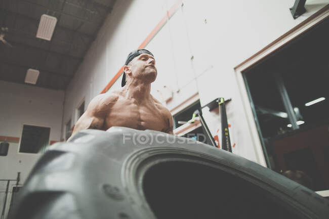 Низкий угол обзора мускулистого человека, поднимающего большую шину в спортзале — стоковое фото