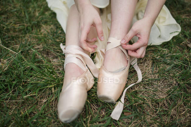 Vista da vicino della ballerina che lega i nastri della sua scarpa da punta sull'erba — Foto stock
