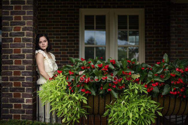 Belle jeune femme debout sur un porche ombragé rempli de fleurs — Photo de stock