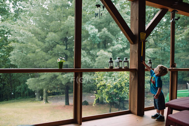 Um menino pequeno alcança para um swatter da mosca em uma tela no porch. — Fotografia de Stock