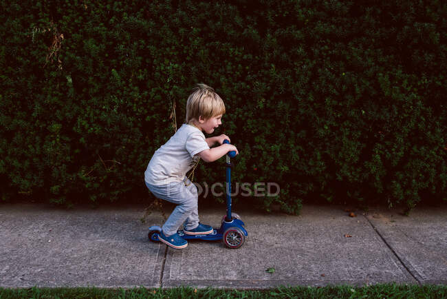 Un petit garçon monte son scooter sur le trottoir. — Photo de stock