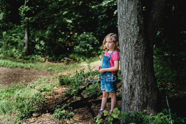 Ein kleines Mädchen steht neben einem Baum auf einem Bauernhof. — Stockfoto