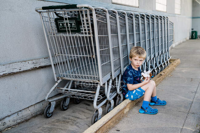 Маленький мальчик дуется рядом с рядом тележек с покупками. — стоковое фото