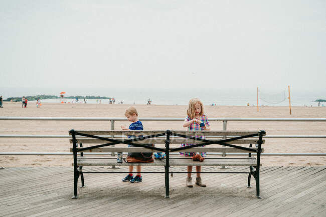 Duas crianças comem sorvete em um calçadão de praia. — Fotografia de Stock