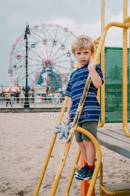 A little boy stands in front of a ferris wheel at Coney Island. — Stock Photo