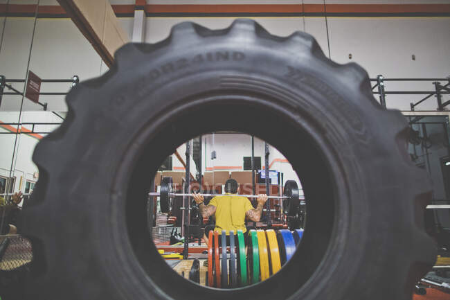 Вид сквозь шины бодибилдера, делающего приседания в спортзале — стоковое фото