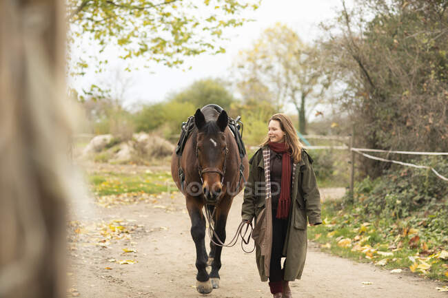 Jeune cavalière avec un cheval à l'extérieur marchant — Photo de stock