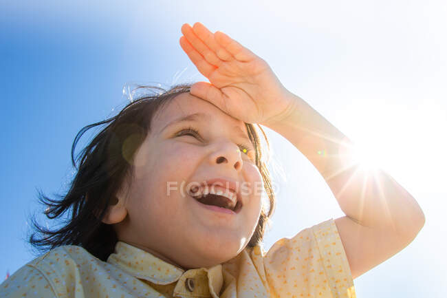 Felice ragazzo sorridente in bagliore sole con mano sulla fronte — Foto stock