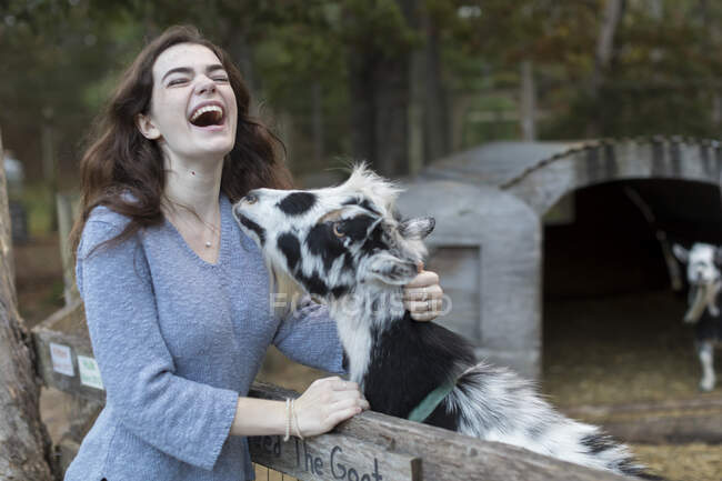Teenage girl laughing while petting goat in farm setting — Stock Photo