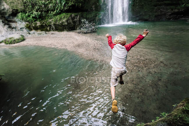 Vista desde arriba del niño en edad preescolar saltando al agua en Nueva Zelanda - foto de stock
