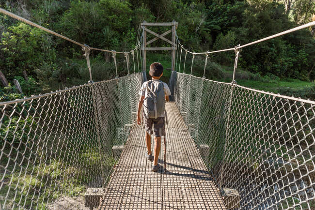 Tween menino com mochila andando na ponte de madeira — Fotografia de Stock