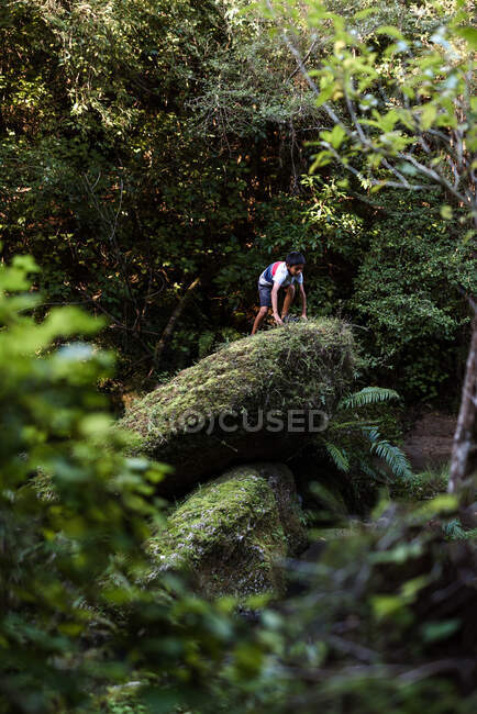 Preteen boy climbing on green rocks in forest — Stock Photo
