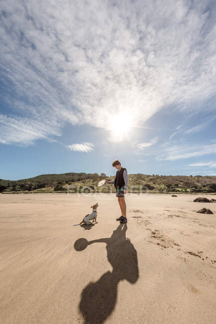 Teen boy playing with dog at beach — Stock Photo