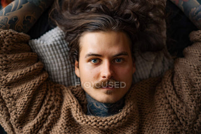 Bonito tatuado sexy homem com cabelos longos e bigode no sofá — Fotografia de Stock