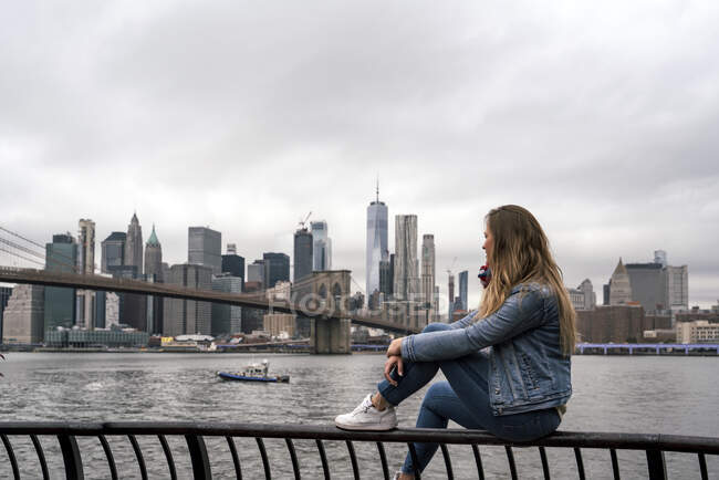 Приваблива молода жінка спостерігає за Бруклінським мостом з річки Гудзон (Нью - Йорк). — стокове фото