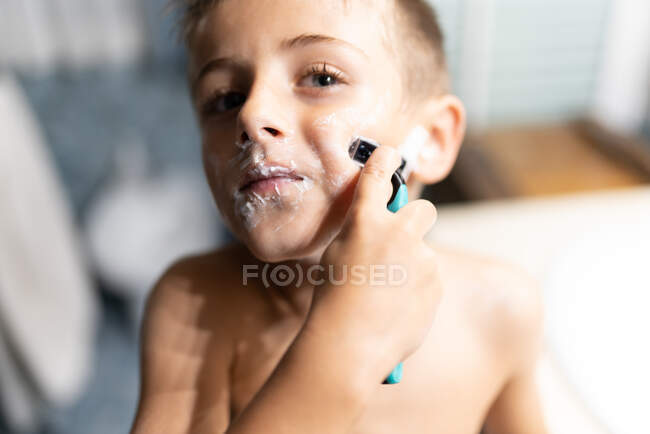 Niño afeitándose como un adulto en el baño delante del espejo - foto de stock