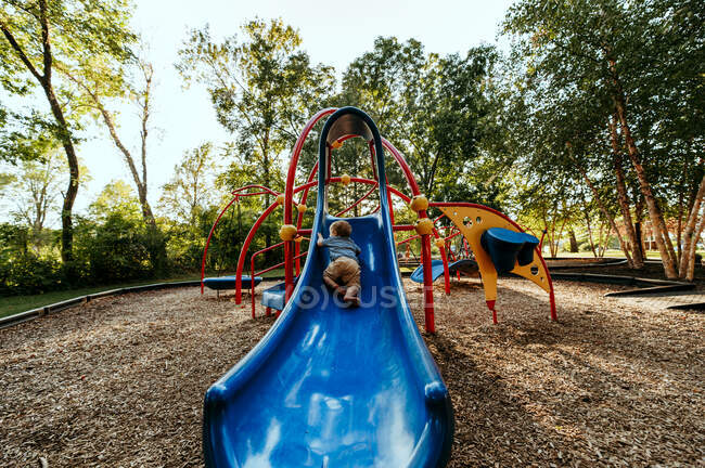 Малыш карабкается по синей горке в парке — стоковое фото