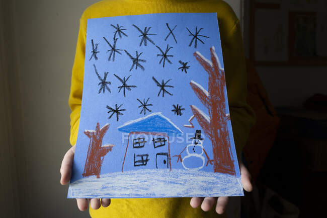 Крупним планом дитина тримає масляний пастельний малюнок засніженої зимової сцени — стокове фото