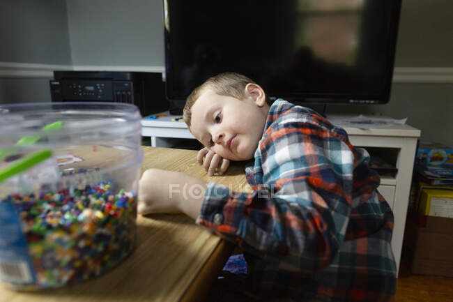 Menino em idade pré-escolar calmamente coloca a cabeça na mesa enquanto faz projeto de artesanato — Fotografia de Stock