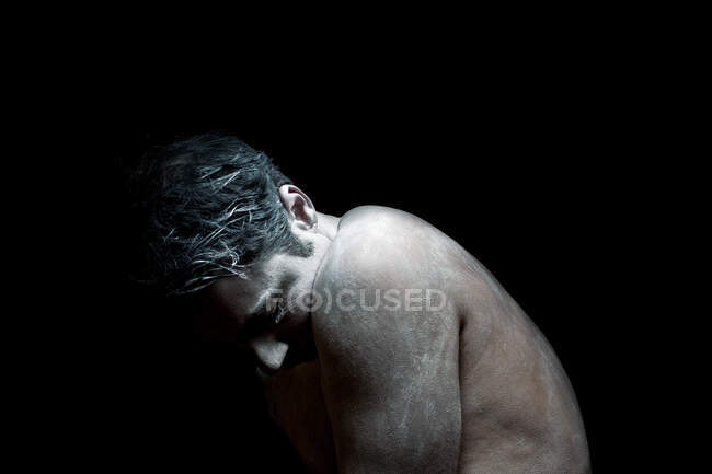 Hombre desnudo cubierto de pintura blanca mirando hacia abajo - foto de stock