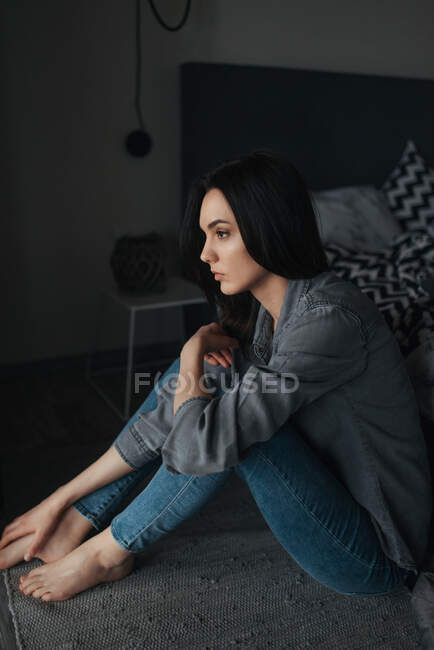 Una joven mujer solitaria sentada en el suelo en una habitación oscura - foto de stock
