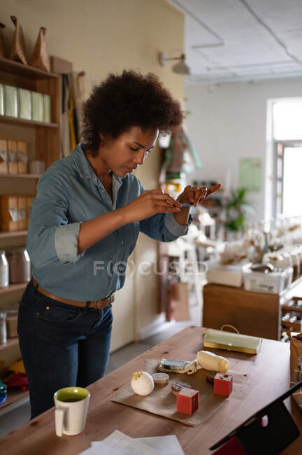 Mujer de raza mixta disparando cosmética orgánica para el blog durante el trabajo en la tienda ecológica - foto de stock