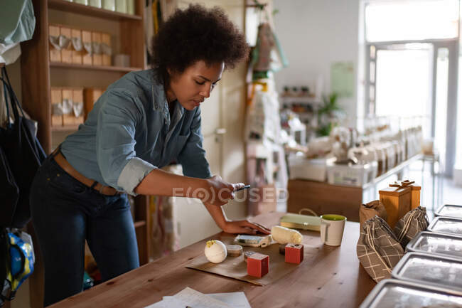 Vendedor étnico atirando ecologicamente limpo cosmético para blog durante o trabalho na loja — Fotografia de Stock