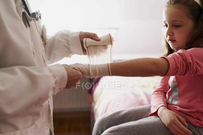 Женщина-врач перевязывает руку маленькой девочке в своей комнате. Концепция врача — стоковое фото