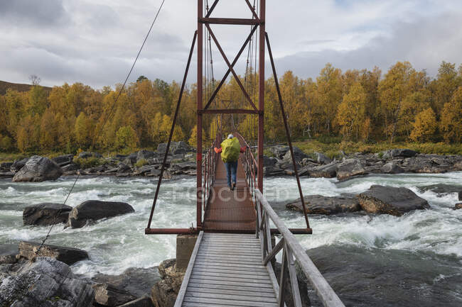 Escursionista che attraversa il ponte sospeso sul fiume Lajsso lungo il Kungsleden Trail, Lapponia, Svezia — Foto stock