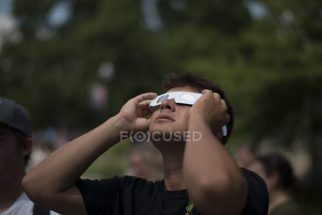 Young man looking up at solar eclipse wearing paper protective glasses — Stock Photo