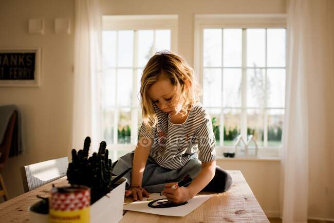 Chica joven dibujando en casa con pluma en la cara y las manos - foto de stock