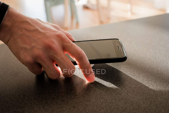 Mão de homem segurando um telefone na cozinha em casa — Fotografia de Stock