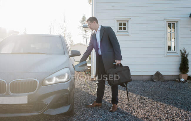 Чоловік вимикає свій електричний автомобіль, виходячи з дому, щоб їхати на роботу — стокове фото