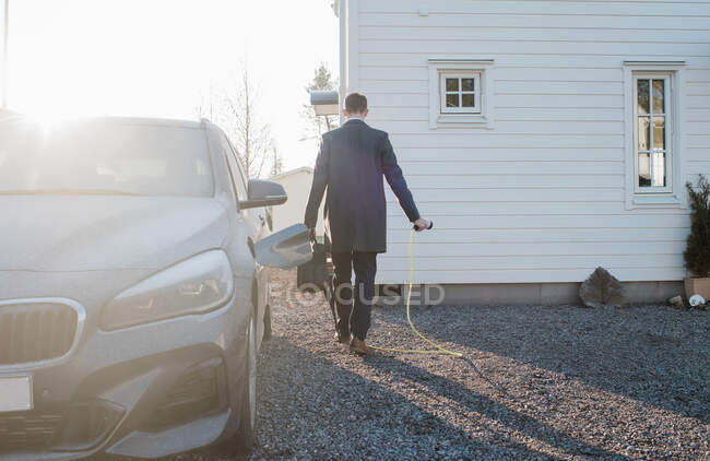 Hombre caminando con el plomo eléctrico del coche que sale para el trabajo en la mañana - foto de stock