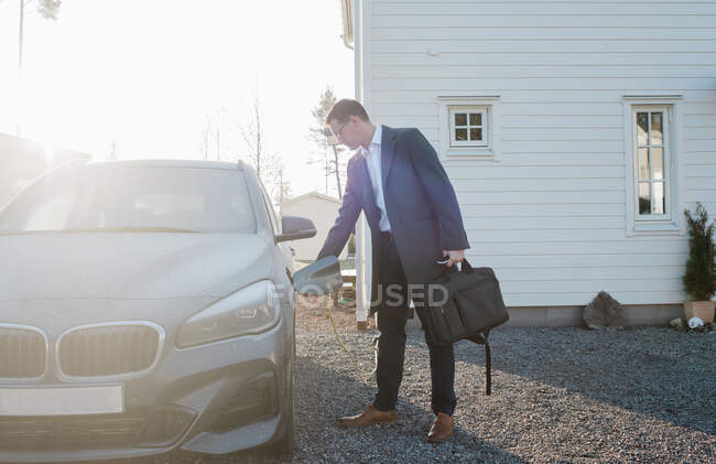 Man unplugging his electric car ready to leave for work from home — Stock Photo