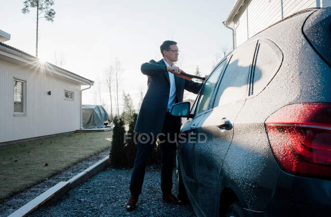 Hombre de negocios raspando hielo de su coche en la mañana antes del trabajo - foto de stock