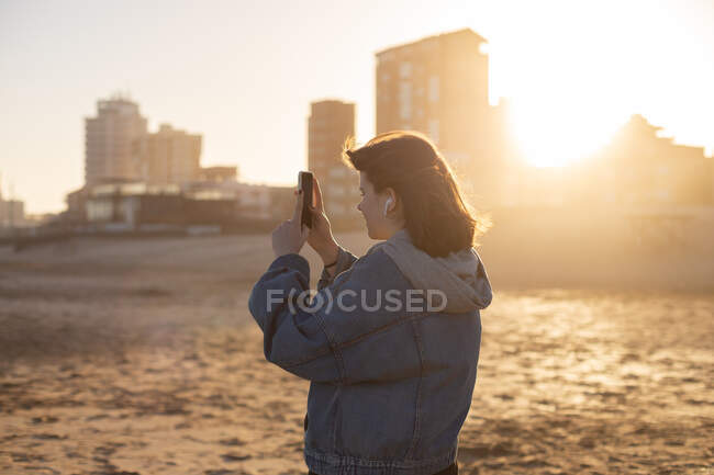 Chica toma fotos en el teléfono de la puesta del sol en la playa del océano Atlántico - foto de stock