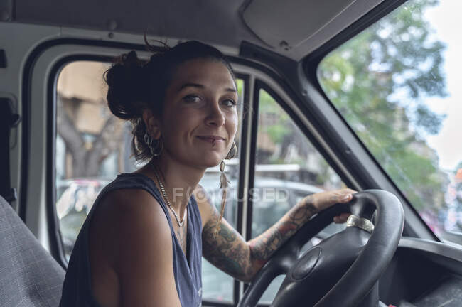Giovane donna, con tatuaggi e piercing, alla guida di un furgone, guarda la stanza con espressione soddisfatta. — Foto stock