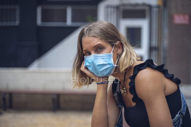 Beautiful girl, with a face mask looks towards the camera, with tired and disgusted face. — Stock Photo