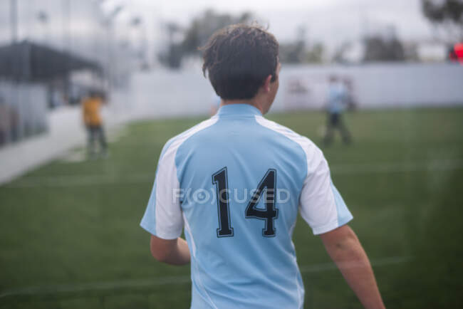 Ragazzo adolescente che gioca a calcio al coperto indossando maglia azzurra numero 14 — Foto stock