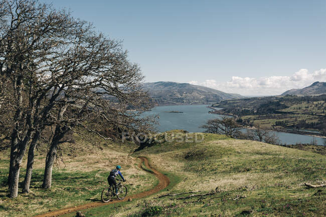 A young woman bikes along a trail overlooking the Columbia River. — Stock Photo