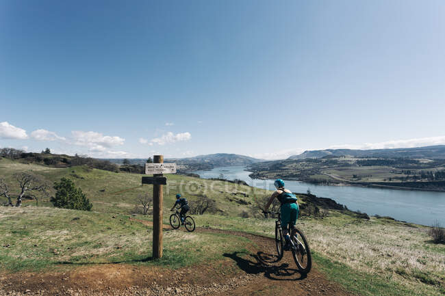 Due ragazze in bicicletta lungo un sentiero che si affaccia sul fiume Columbia. — Foto stock