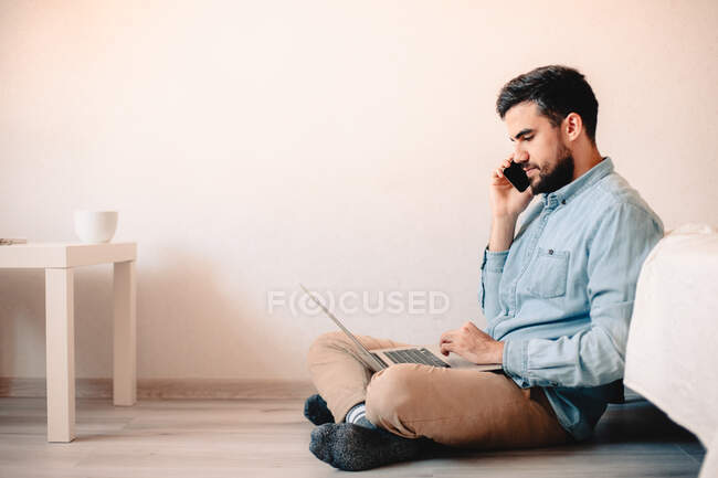Человек разговаривает на смартфоне, используя ноутбук — стоковое фото