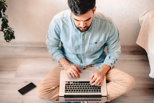 Молодий чоловік використовує ноутбук, сидячи на підлозі вдома — стокове фото