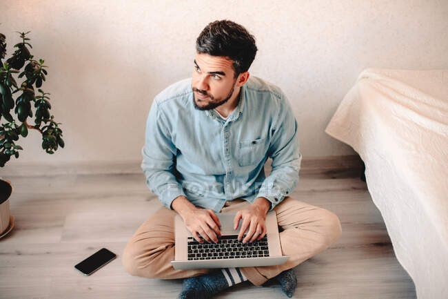 Homem usando computador portátil enquanto sentado no chão em casa — Fotografia de Stock