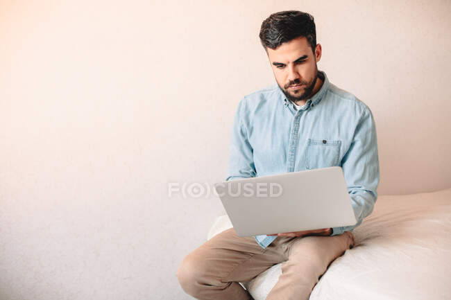 Young man using laptop computer while sitting on bed at home — Stock Photo