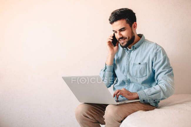 Happy businessman talking on smart phone while using laptop computer — Stock Photo
