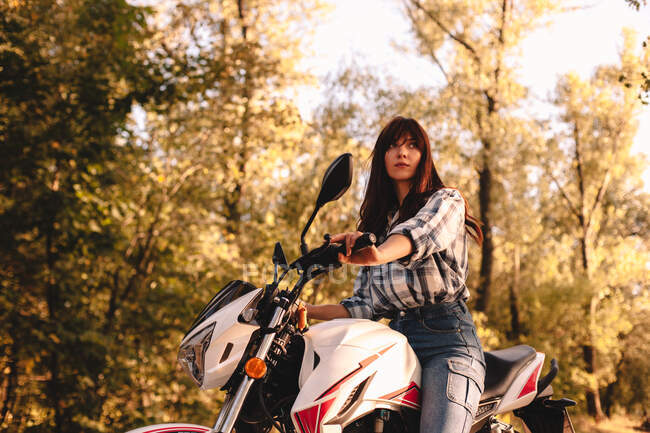 Fiduciosa giovane donna in sella alla moto tra gli alberi nella foresta — Foto stock