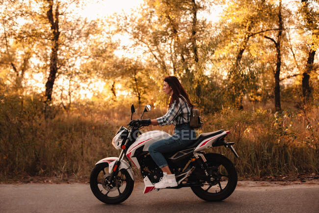 Jovem mulher confiante andando de moto na estrada rural ao pôr do sol — Fotografia de Stock